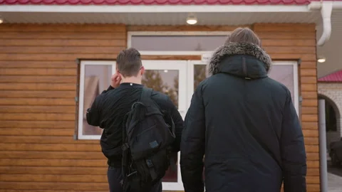 Two young men wearing winter jackets walked into a wooden building with glass Stock Footage 321413669