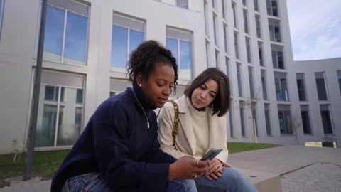Two young multiracial female worker standing on street using and looking mobile Stock Footage 267484773