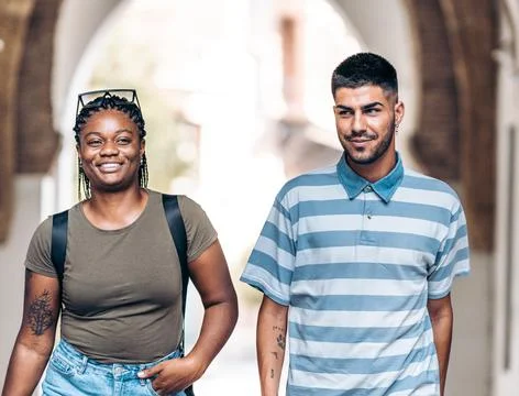 Two young people of different ethnicities smiling as they stroll through a city Stock Photos