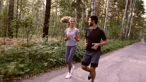 Two young people jogging together in the park full of green trees Stock-Footage 68056926