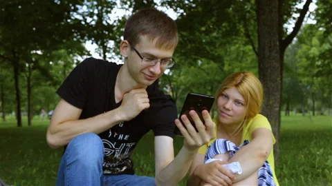 Two young people look closely at the smartphone. The guy has a smile, the girl i Stock Footage 101614494