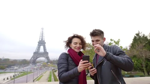 Two young people is looking on screen of mobile phone in background of Eiffel Stock Footage 98810331