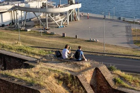 Two young people relaxing on a grassy hill near a riverbank Stock Photos