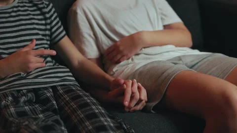 Two young people sit on a sofa, wearing casual home clothes, offering each .. Stock Footage 304448773