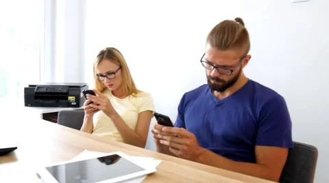 Two young people sitting behind the table and using their mobile phones Stock Footage 54931204