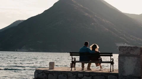 Two young people sitting on a bench at sunset by the sea Montenegro Stock Footage 229982022