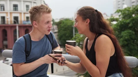 Two young people talking, drinking coffee and using smartphone at urban street Stock Footage 93004987