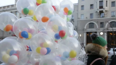 Two young people in warm clothes walk past with a huge bunch of air gel balls. A Stock Footage 86774976