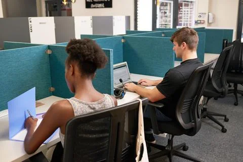 Two young people work side by side in office with desk dividers, coworking Stock Photos