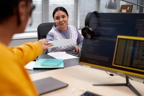 Two young people working in IT development and handing documents across table 스톡 사진