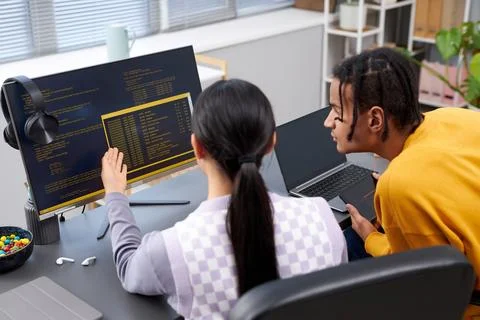 Two young people writing code in office and pointing at computer screen Fotos Stock