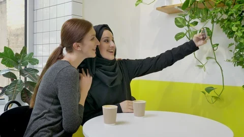 Two young pretty womans sitting in cafe, one of them muslim woman in hijab Stock Footage 90610709
