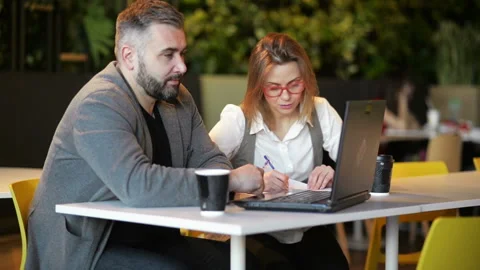 Two Young Professionals Sitting at Desk, Looking at Laptop Screen and Discussing Stock Footage 106345540