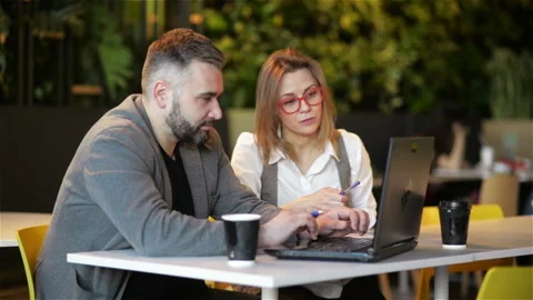 Two Young Professionals Sitting at Desk, Looking at Laptop Screen and Discussing Stock Footage 106346212