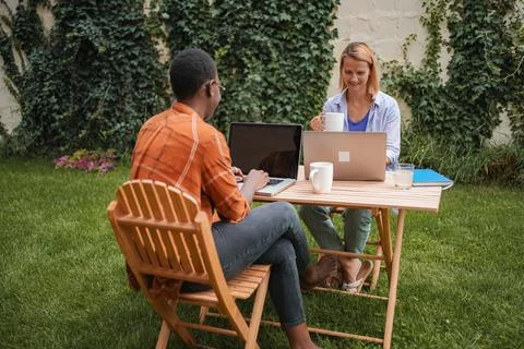 Two young professionals working remotely on laptops in a garden Stock Photos