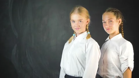 Two young school girls in class on the background of blackboard.  Vídeo Stock 136506829