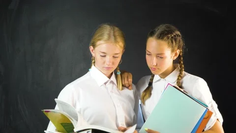 Two young school girls in class holding text books  Stock Footage 136507729