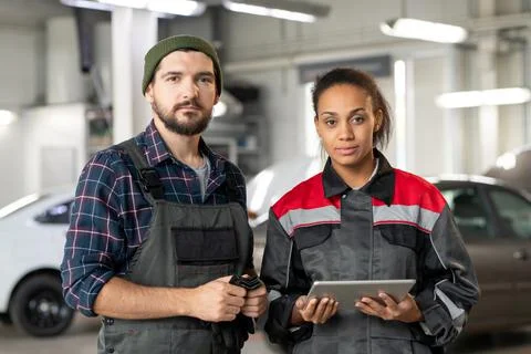 Two young serious intercultural workers of car maintenance center in workshop Stock Photos