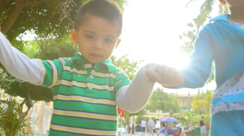 Two young siblings hold hands as they walk down the street with their parents Stock Footage 33891953