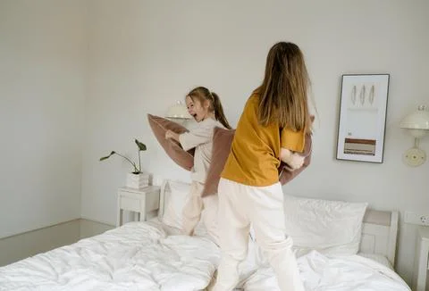 Two young sisters are having a pillow fight on a bed, their laughter echoing  Stock Photos