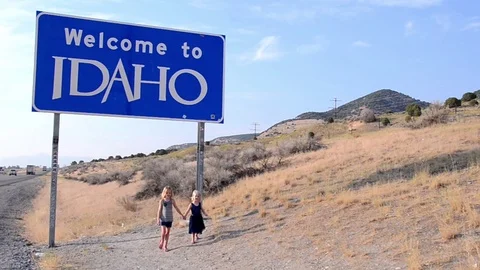 Two young sisters holding hands next to Idaho state border sign 스톡 동영상 94683539