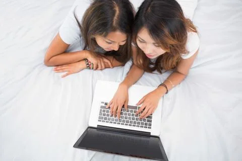 Two young sisters lying on a bed using laptop Photos