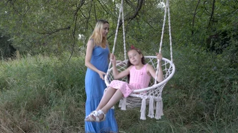 Two young sisters play and swing on a suspended swing in the park, outdoors o 스톡 동영상 114834545