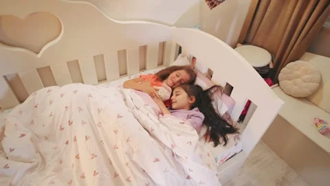 Two young sisters sleeping peacefully in a cozy bedroom during a sunny afternoon Stock Footage 317654798