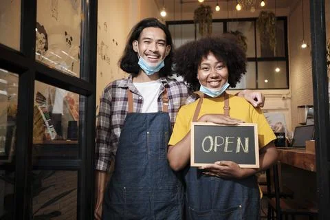 Two young startup barista partners stand at casual cafe door, write and show Stock Photos