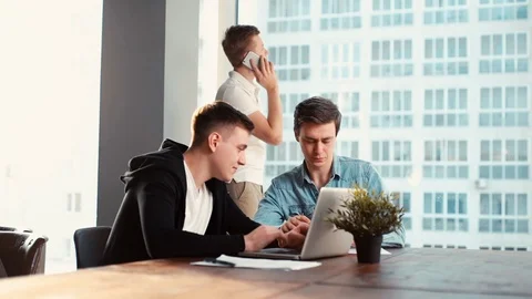 Two young startupers discussing project together at the table with laptop i Stock Footage 121556509