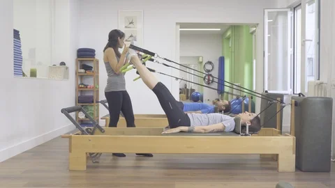 Two young students and instructor working their lower body with a reformer bed Stock Footage 126975306