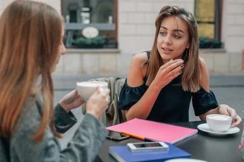 Two young students are talking at the cafe restaurant. Outdoor background. Stock Photos