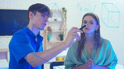 Two young students draw geometric shapes on glass with a marker and look at them 写真素材