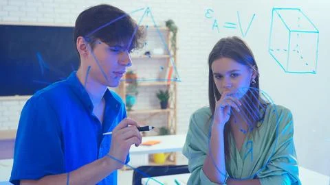 Two young students draw geometric shapes on glass with a marker and look at them 写真素材