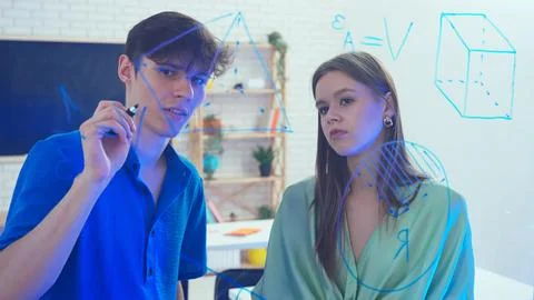 Two young students draw geometric shapes on glass with a marker and look at them 写真素材