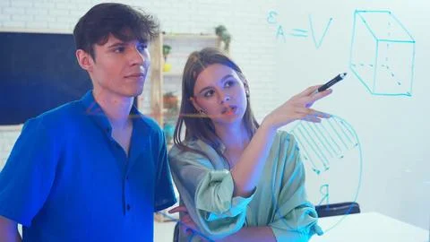 Two young students draw geometric shapes on glass with a marker and look at them 写真素材