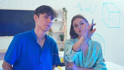 Two young students draw geometric shapes on glass with a marker and look at them 写真素材