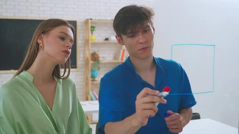 Two young students draw math problems on the glass with a marker and look at Stock Footage 282089425