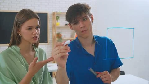 Two young students draw math problems on the glass with a marker and look at Stock Photos