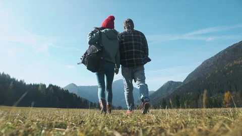 Two young travellers walking back in front of grass. Couple trekking and holding Stock Footage 144219980