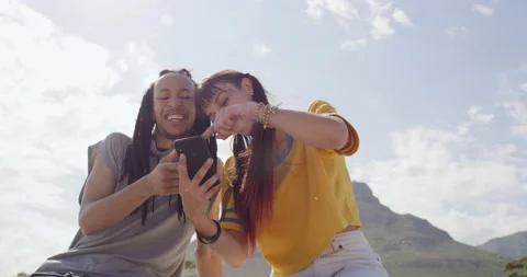 Two young trendy friends using phone and talking at skate park, relaxing with Vidéo 198420976