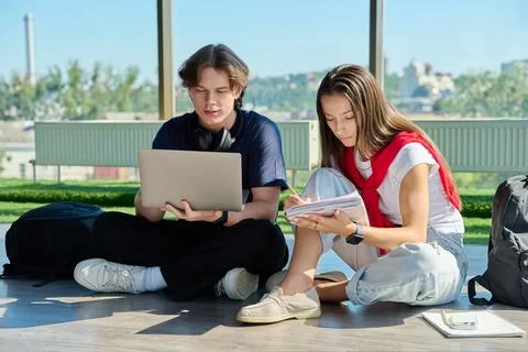 Two young university students sitting on floor studying using laptop and writing Stock Photos