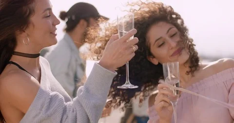 Two young women dancing back to back, with glasses in their hands and friends Stock Footage 81212316