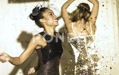 Two young women dancing with confetti falling. Stock Photos