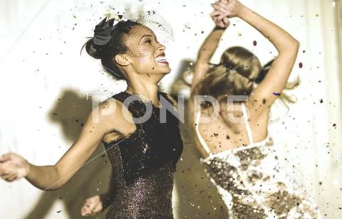 Two young women dancing with confetti falling. Stock Photos