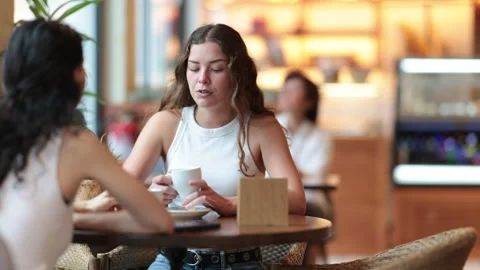 Two young women drinking coffee and talking in cafe Stock Footage 332737067