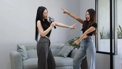Two young women having fun together, standing dancing and singing using a Stock Footage 340232140