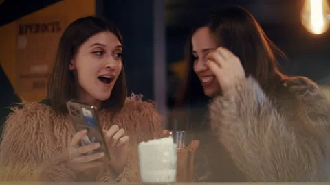 Two young women laughing while using smartphone at bar Stockbeeldmateriaal 319772569