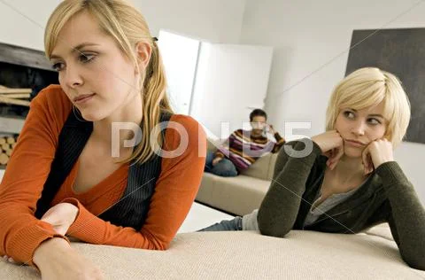 Two young women looking serious with a young man sitting in the background Stock Photos