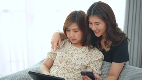 Two young women sitting on couch using digital tablet and smartphone for br.. Video stock 342781681